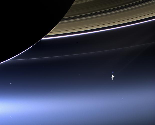 A photo In the top left corner a part of saturn and its rings. Below, in the centre a tiny bright spot, marked with an arrow.