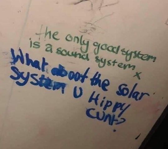 Green marker writing on a bathroom wall: "The only good system is a sound system." Below, in blue marker: "What about the solar system, u hippie cunt?"