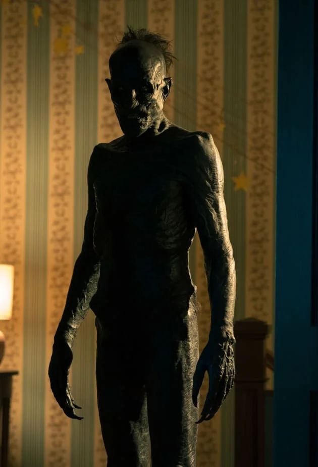 Eine dunkle Figur steht in einem Raum, im Hintergrund eine gestreifte Tapete. Man kann die Figur nicht ganz klar erkennen. Es handelt sich scheinbar um einen abgemagerten älteren Mann mit schwarzer, schrumpliger aber leicht glänzender Haut ohne Bekleidung. Seine Hände sind übernatürlich riesig. Haare wachsen wirr an seinem Hinterkopf. Mich erinnert er an eine Moorleiche. Es handelt sich um den Nachtschreck George aus der im Post erwähnten Fernsehserie "Evil".