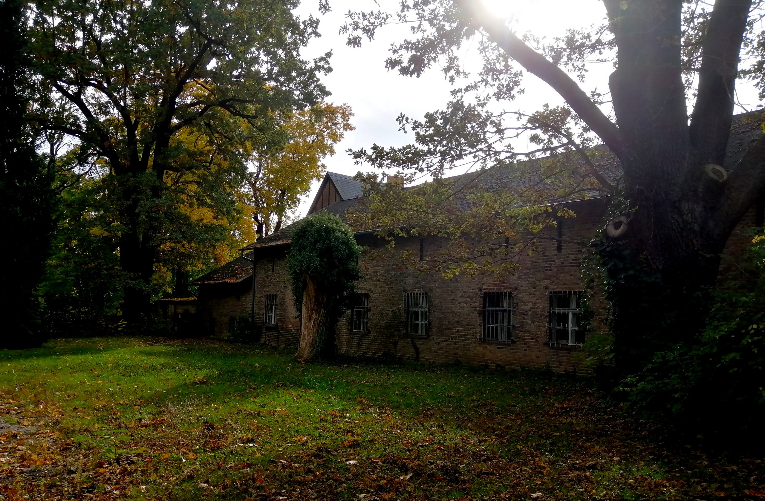 Ein langgezogenes 2-stöckiges Haus aus gelb-grauen Ziegeln. Die Fenster im Erdgeschoss sind vergittert, oben sind es Schlitze, wie Schießscharten, Es wirkt ein wenig heruntergekommen, ist aber keine Ruine. Es steht auf einer Wiese, mit Bäumen ringsum.