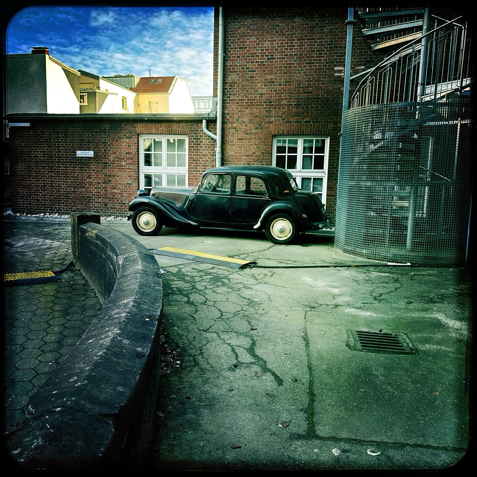 ein hinterhof, moderne feuertreppe. davor parkt ein schwarzer historischer citroën 11er. ein wenig blauer himmel. die sonne scheint.