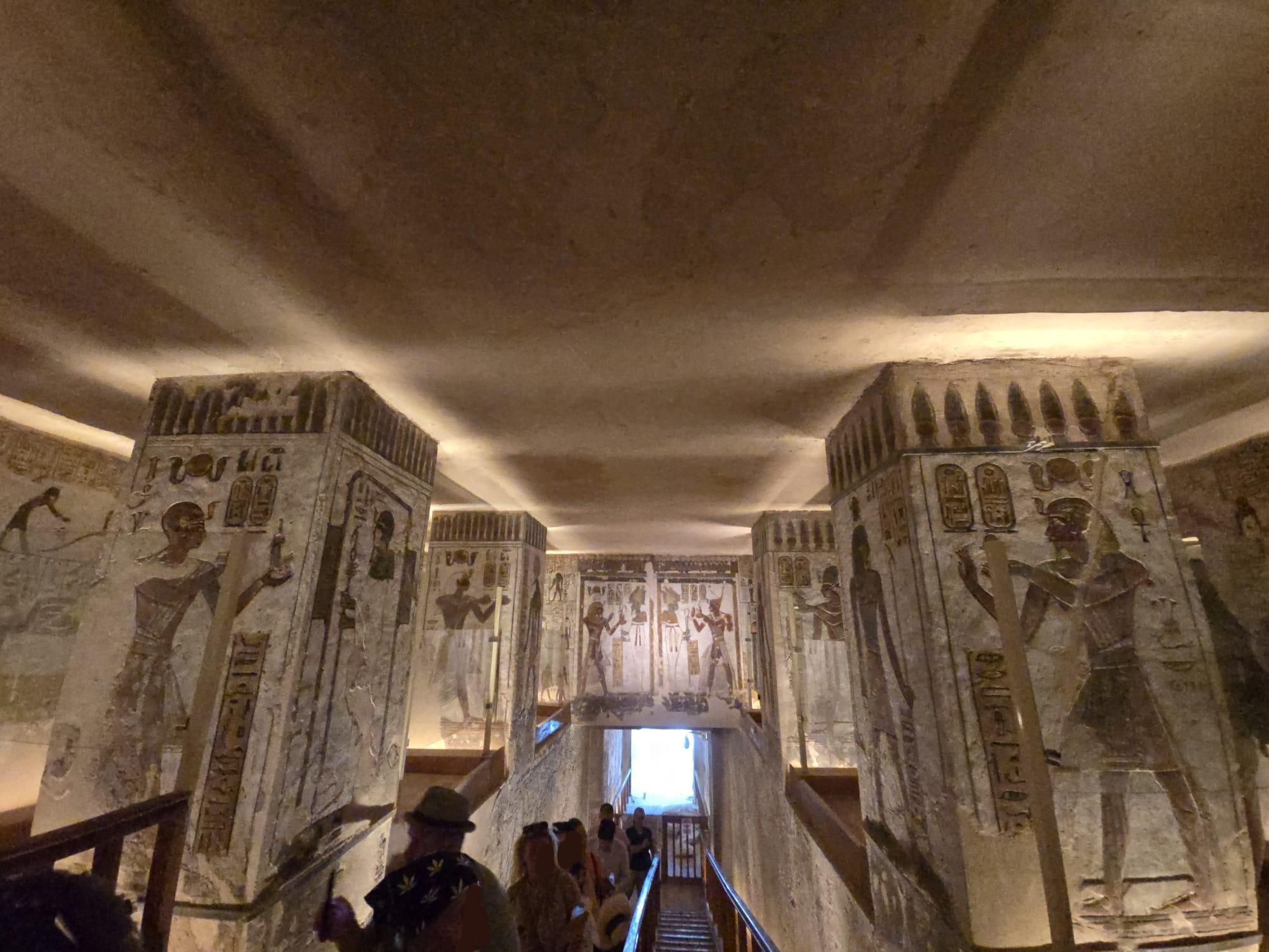 Einige Menschen in einem Raum mit Treppe, einem überbelichteten Kellerraum, mehreren Säulen und hölzernem Gitter. Markant sind die Zeichnungen und Hieroglyphen an quasi allen freien Flächen mit Ausnahme der weiß-bräunlich gebliebenen Decke. Weitere Infos zum Bild (Aufnahmeort) nach Runden-Ende